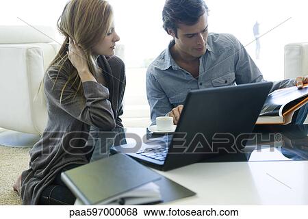 Couple sitting together at coffee table, looking at book View Large Photo Image Stock Photo - Couple sitting together at coffee table, looking at book. Fotosearch