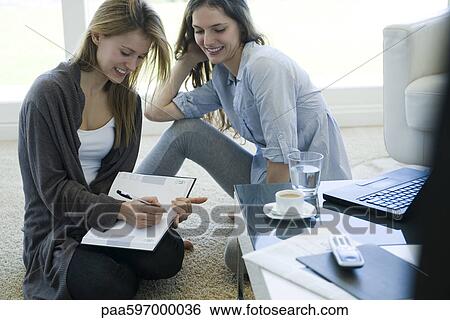 Friends sitting together in living room, one writing in agenda View Large Photo Image Stock Photograph - Friends sitting together in living room, one writing in agenda. Fotosearch