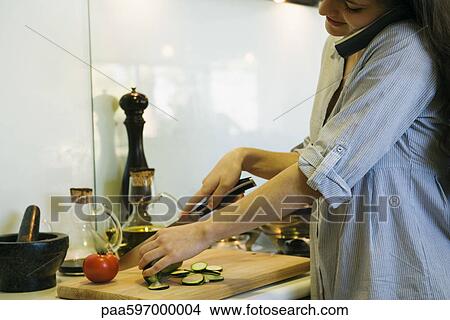 Woman talking on phone while chopping vegetables View Large Photo Image Picture - Woman talking on phone while chopping vegetables. Fotosearch