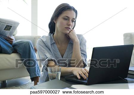 Young woman sitting at coffee table, using laptop computer View Large Photo Image Stock Photo - Young woman sitting at coffee table, using laptop computer. Fotosearch