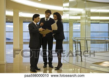 Business executives standing together discussing document View Large Photo Image Stock Image - Business executives standing together discussing document. Fotosearch