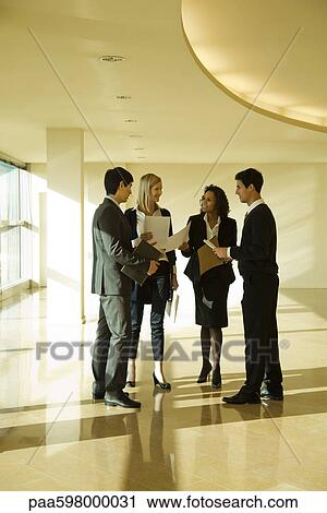 Stock Image - Business executives standing together discussing documents. Fotosearch
