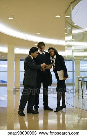 Business executives standing together discussing document View Large Photo Image Stock Image - Business executives standing together discussing document. Fotosearch