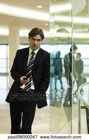 Businessman leaning against glass wall, using cell phone View Large Photo Image Stock Photo - Businessman leaning against glass wall, using cell phone. Fotosearch