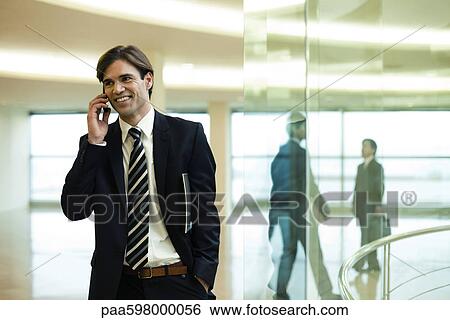 Businessman talking on cell phone in lobby View Large Photo Image Stock Photograph - Businessman talking on cell phone in lobby. Fotosearch