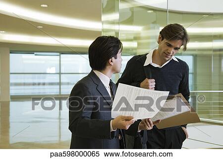 Colleagues discussing documents in corridor View Large Photo Image Stock Photography - Colleagues discussing documents in corridor. Fotosearch