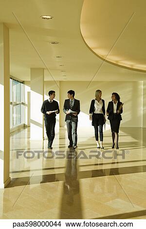 Group of business associates talking as they walk together in lobby View Large Photo Image Picture - Group of business associates talking as they walk together in lobby. Fotosearch