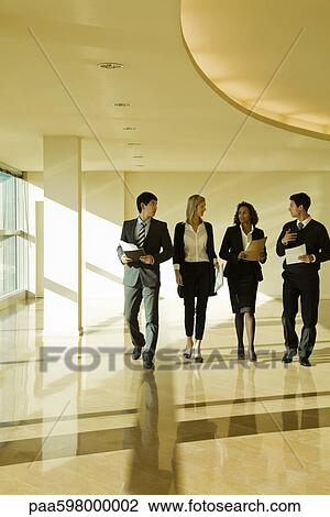 Stock Image - Group of executives talking as they walk together in lobby. Fotosearch