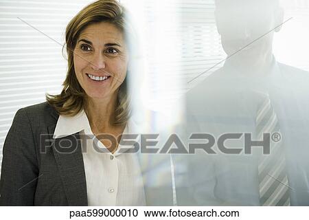 Smiling businesswoman looking away, businessman behind glass wall View Large Photo Image Stock Image - Smiling businesswoman looking away, businessman behind glass wall. Fotosearch