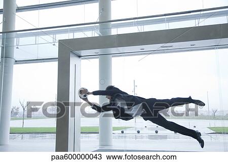 Stock Image - Businessman catching soccer ball in lobby. Fotosearch