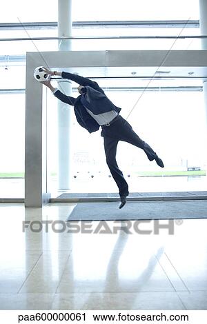 Stock Image - Businessman catching soccer ball in lobby. Fotosearch