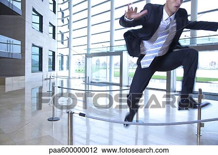 Stock Image - Businessman jumping over ropes in lobby. Fotosearch