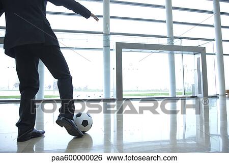 Stock Photograph - Businessman kicking soccer ball in lobby. Fotosearch