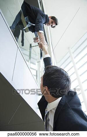 Businessman leaning over balcony, holding on to colleague's hand View Large Photo Image Stock Photograph - Businessman leaning over balcony, holding on to colleague's hand. Fotosearch