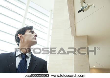 Businessman looking up at security camera View Large Photo Image Stock Image - Businessman looking up at security camera. Fotosearch