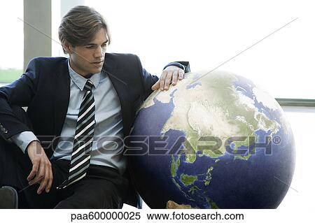 Stock Photography - Businessman sitting next to ball in lobby. Fotosearch