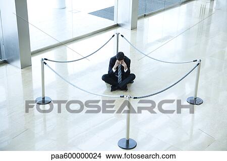 Picture - Businessman sitting on floor inside roped off area in lobby. Fotosearch