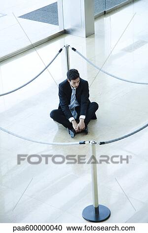 Stock Image - Businessman sitting on floor inside roped off area in lobby. Fotosearch