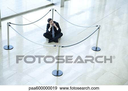 Stock Photo - Businessman sitting on floor inside roped off area in lobby. Fotosearch