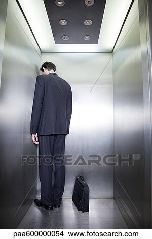 Picture - Businessman standing in corner of elevator with back to camera and head down. Fotosearch