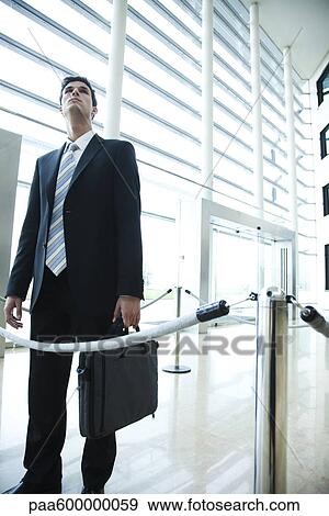 Stock Photo - Businessman standing in lobby, looking up. Fotosearch