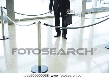 Stock Photo - Businessman standing inside roped off area in lobby. Fotosearch