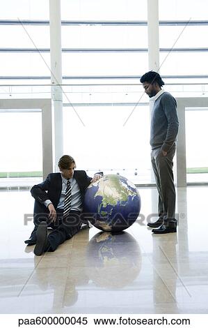 Stock Photography - Businessmen contemplating ball in lobby. Fotosearch