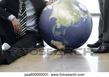 Stock Image - Businessmen contemplating ball. Fotosearch