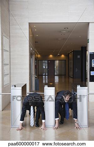 Stock Photo - Businessmen crouching in starting position in lobby turnstiles. Fotosearch
