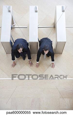 Stock Photography - Businessmen crouching in starting position in lobby turnstiles. Fotosearch