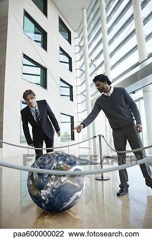 Businessmen looking at ball in lobby View Large Photo Image Stock Image - Businessmen looking at ball in lobby. Fotosearch