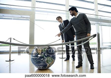 Stock Photo - Businessmen looking at ball in lobby. Fotosearch
