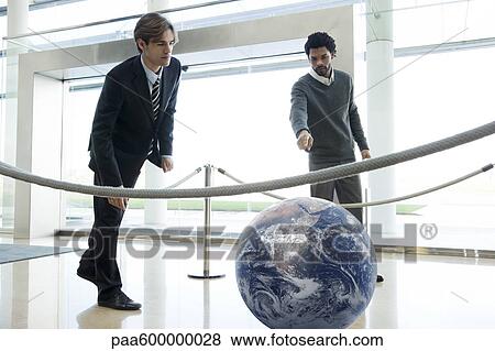 Stock Photo - Businessmen looking at ball in lobby. Fotosearch