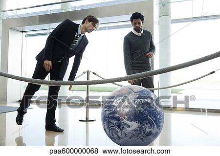 Businessmen looking at ball in lobby View Large Photo Image Stock Photo - Businessmen looking at ball in lobby. Fotosearch