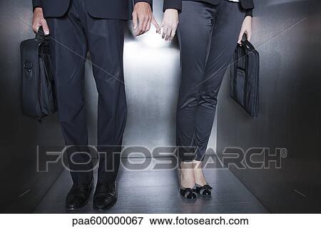 Stock Photo - Colleagues holding hands in elevator, low section. Fotosearch