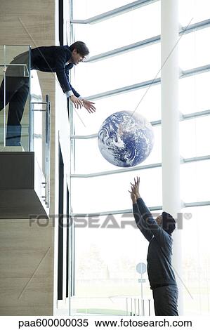 Stock Photography - Colleagues throwing ball in lobby. Fotosearch
