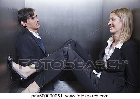 Stock Image - Colleagues trapped in elevator, sitting on floor chatting. Fotosearch
