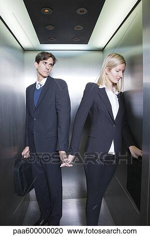 Stock Image - Professionals holding hands in elevator. Fotosearch