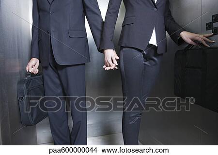 Picture - Professionals holding hands in elevator, cropped. Fotosearch