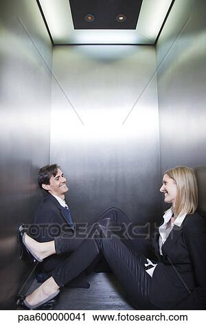 Stock Image - Professionals trapped in elevator, sitting on floor chatting. Fotosearch