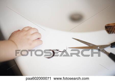 Stock Image - Child's hand resting on sink near scissors and locks of hair. Fotosearch
