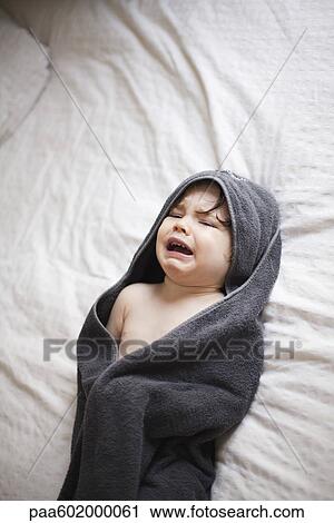 Stock Image - Crying toddler wrapped in a towel after bath. Fotosearch