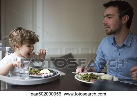 Father and toddler son eating dinner together View Large Photo Image Stock Photograph - Father and toddler son eating dinner together. Fotosearch
