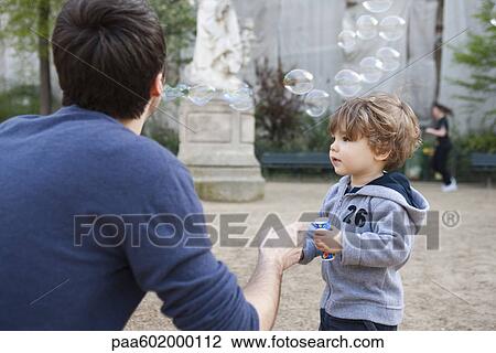 Stock Image - Father and toddler son playing with bubbles. Fotosearch