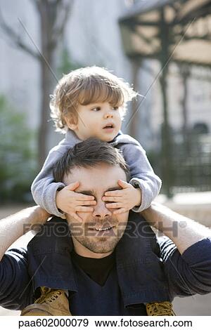 Father carrying toddler son on his shoulders, son covering father's eyes with his hands View Large Photo Image Stock Photo - Father carrying toddler son on his shoulders, son covering father's eyes with his hands. Fotosearch