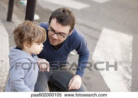 Stock Photography - Father crouching beside toddler son, holding his hand. Fotosearch