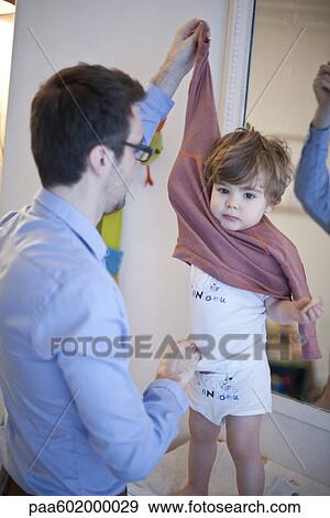Stock Photo - Father helping toddler boy undress. Fotosearch