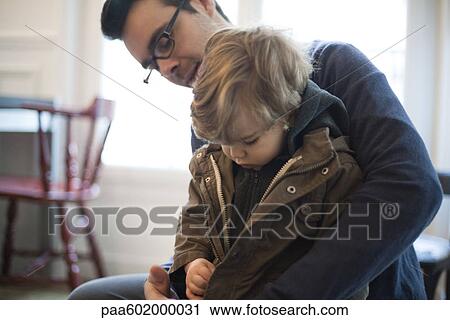 Stock Image - Father helping toddler son zip jacket. Fotosearch