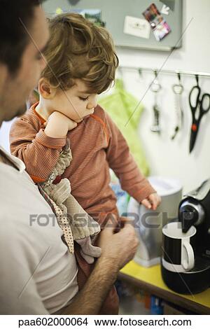 Picture - Father holding young son while preparing espresso. Fotosearch