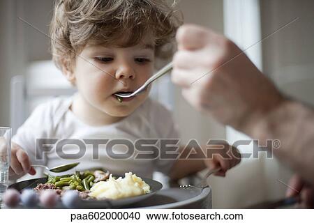 Stock Image - Toddler boy being fed green beans, cropped. Fotosearch